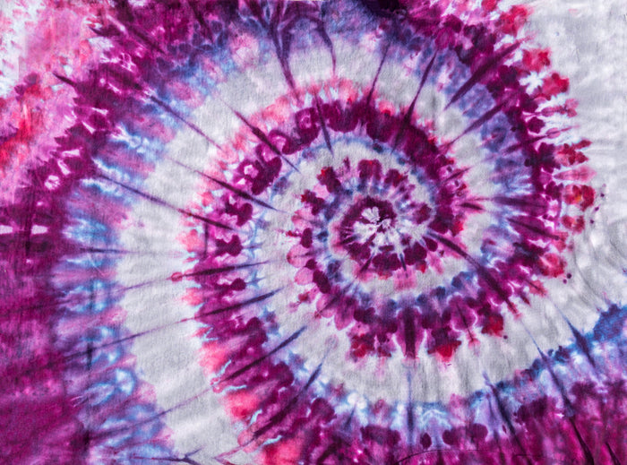 Spiral tie-dye pattern in vivid magenta, purple, blue, and white, radiating outward in a swirling, psychedelic burst of color.