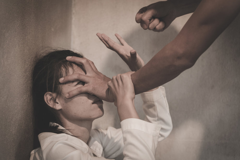 A man pins a cornered woman against a wall by her face, fist raised to strike as she tries to block him.