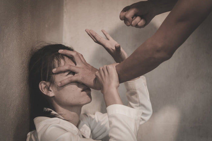 A man pins a cornered woman against a wall by her face, fist raised to strike as she tries to block him.