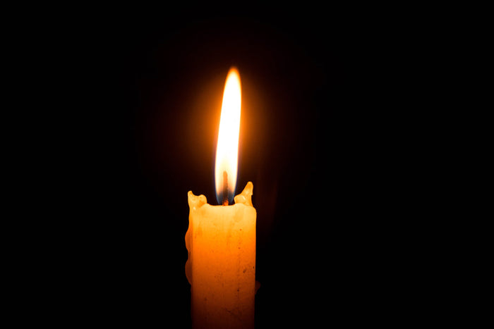 A single lit candle with a tall, steady flame against a solid black background, wax dripping down its side.