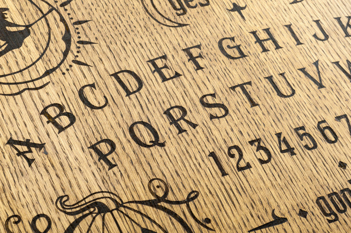 Close-up of a wooden Ouija board showing letters, numbers, and occult symbols used for communicating with spirits.