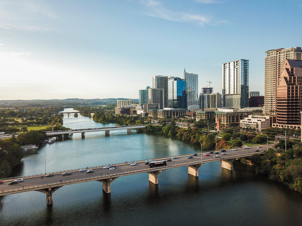 Austin skyline along Lady Bird Lake, with the Congress Avenue Bridge crossing the water beneath downtown high-rises on a clear day.