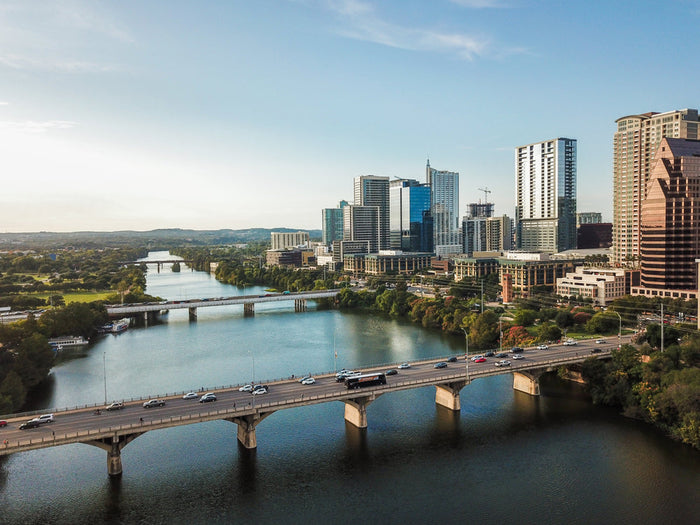 Austin skyline along Lady Bird Lake, with the Congress Avenue Bridge crossing the water beneath downtown high-rises on a clear day.