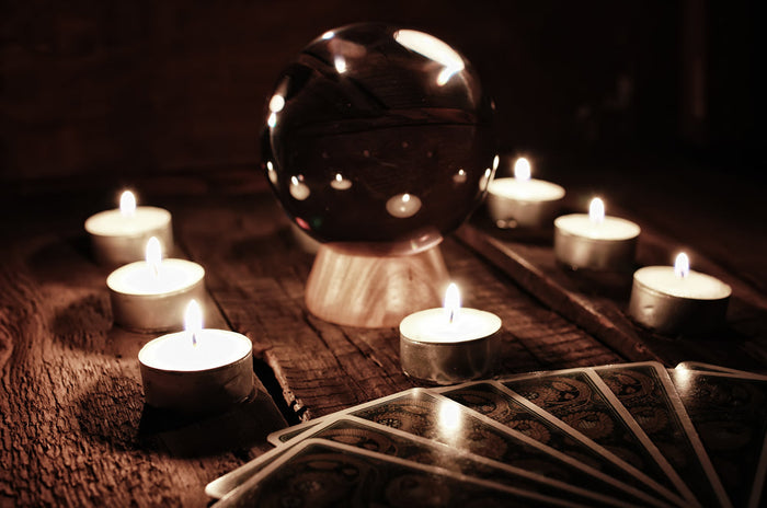 Crystal ball surrounded by glowing candles and fanned tarot cards on a rustic wooden table, creating a dark, mystical fortune-telling scene.